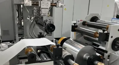 Ultra-precision coating machine applying uniform adhesive coating on industrial material rolls.